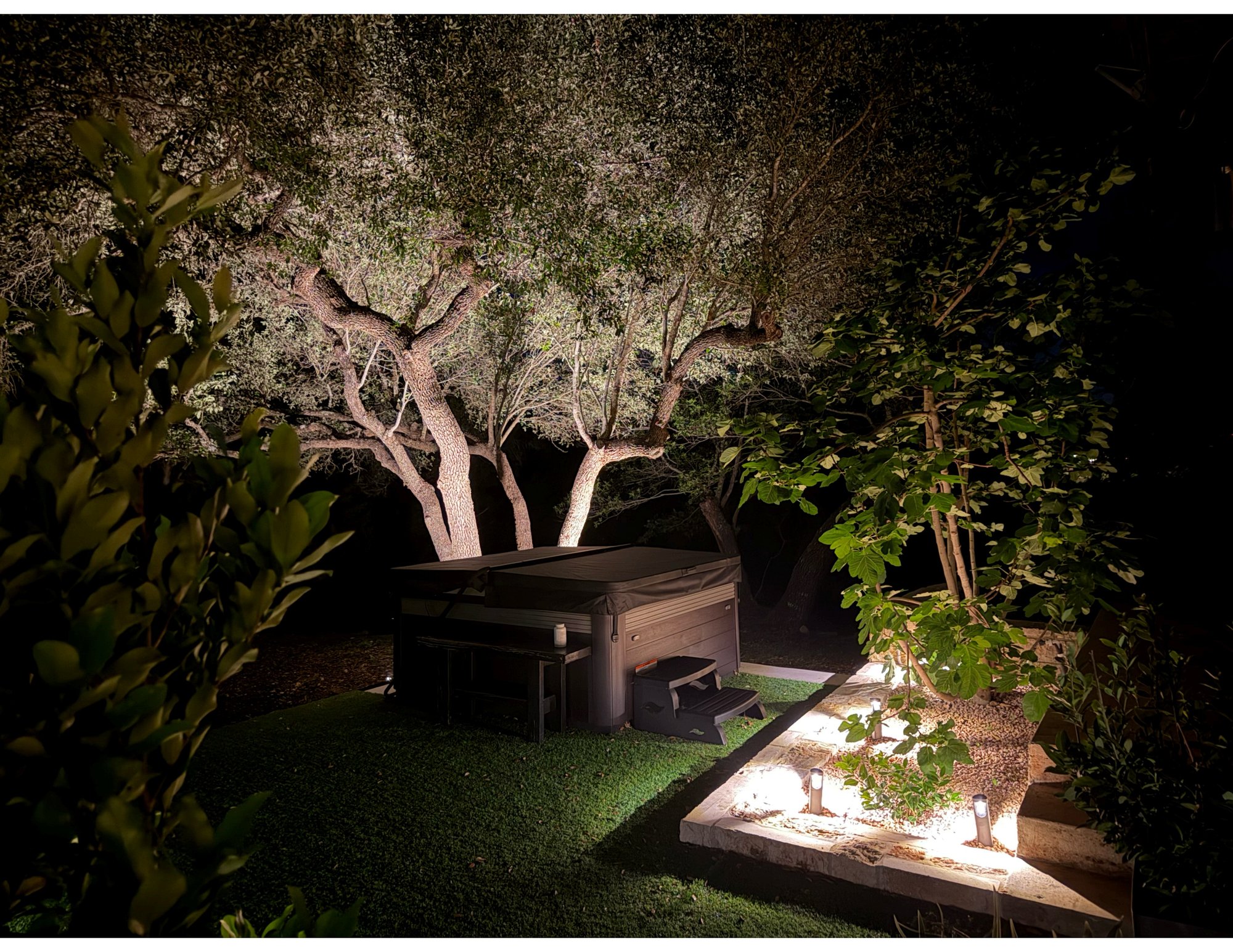 La Paz private hot tub at night, surrounded by uplit live oaks and landscape lighting under the Hill Country sky